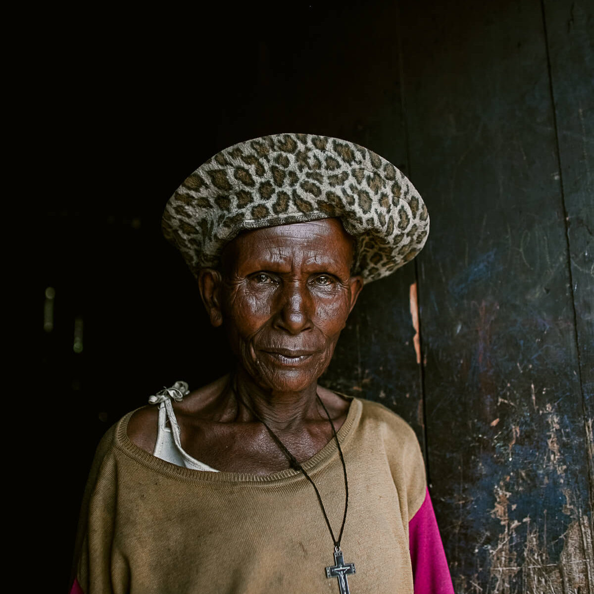 Older woman wearing leopard print hat and crucifix starting directly at the camera