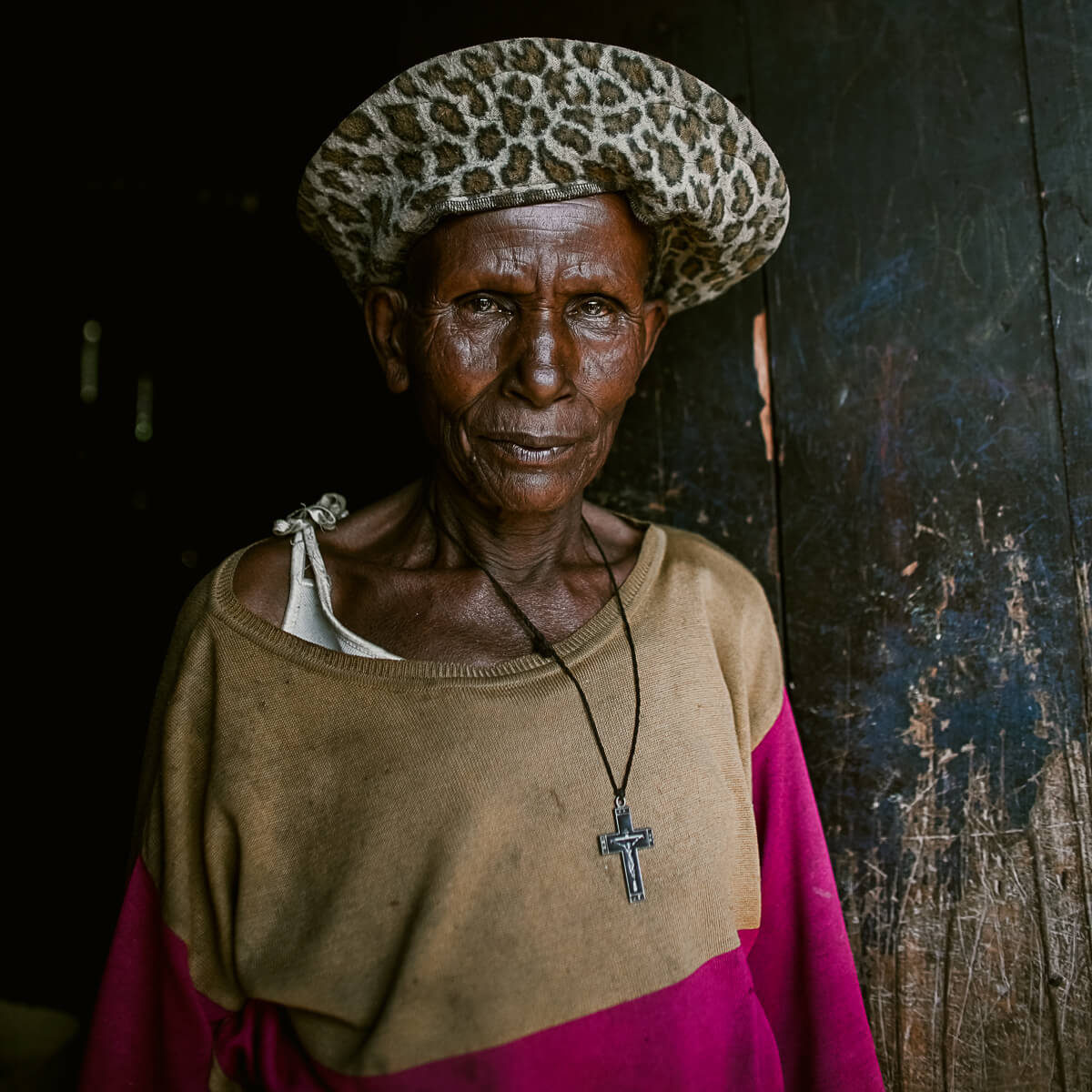 Older woman wearing leopard print hat and crucifix starting directly at the camera